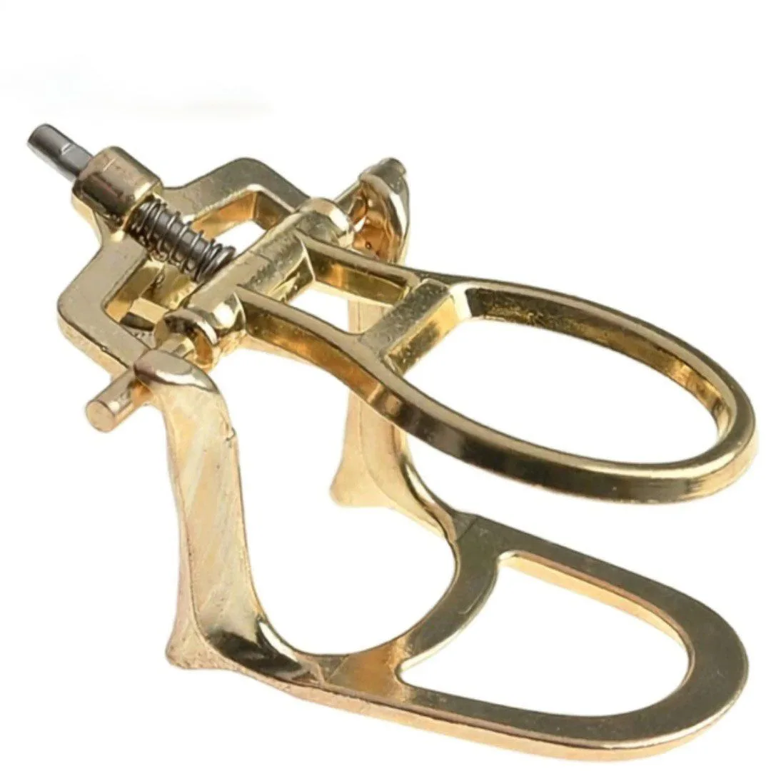Gold-coloured dental articulator frame with oval upper and lower cast supports at right and a rear hinge assembly with a threaded screw and spring at left