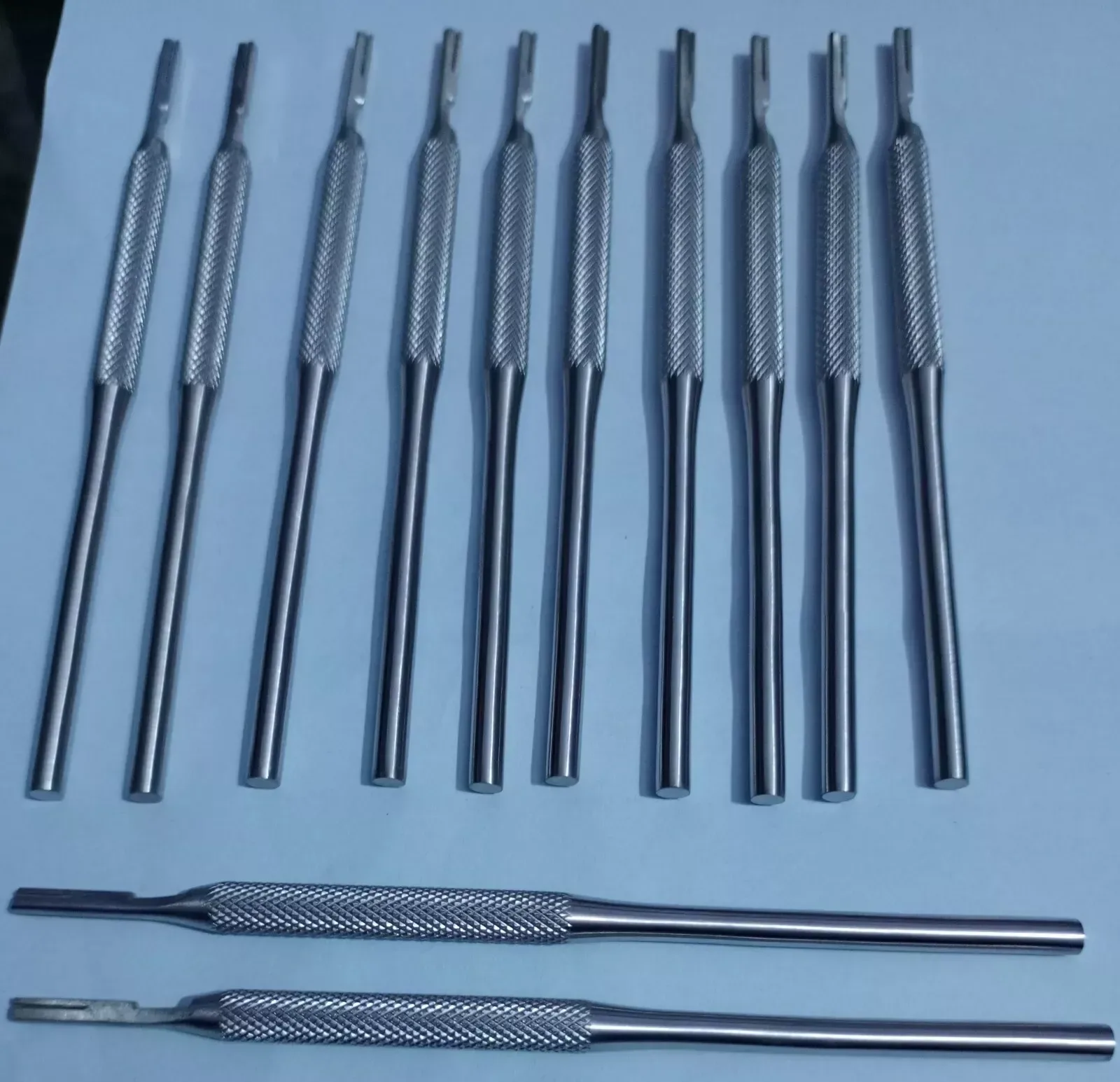 Twelve round knurled reusable scalpel handles without blades, ten upright and two lying horizontally